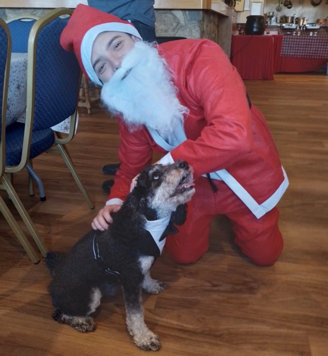 Community member dressed as Santa with a dog at a festive event