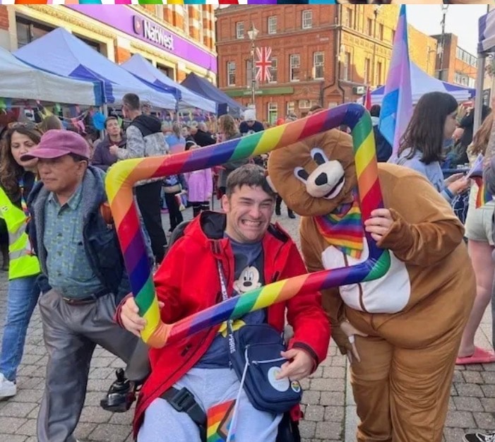 Man in wheelchair smiling at a Pride event with the Healing Hubs bear mascot