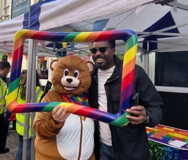Man smiling with the Healing Hubs bear mascot at a Pride event