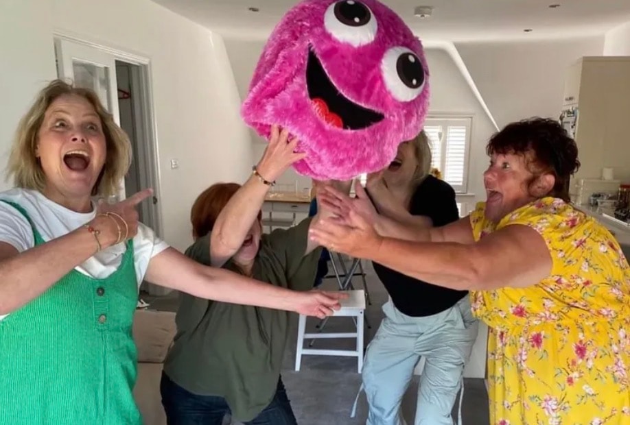 Four women laughing together with a large pink fluffy puppet