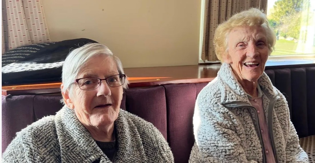 Two elderly women sitting together smiling in a residential lounge