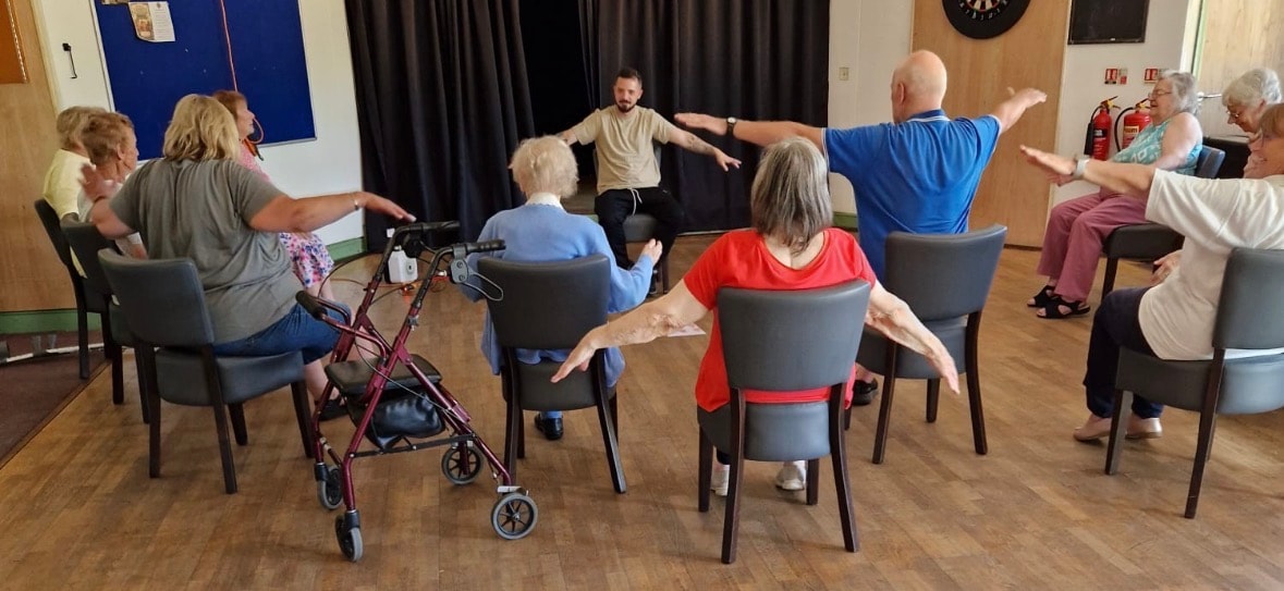 Group of seniors doing seated chair exercises led by an instructor