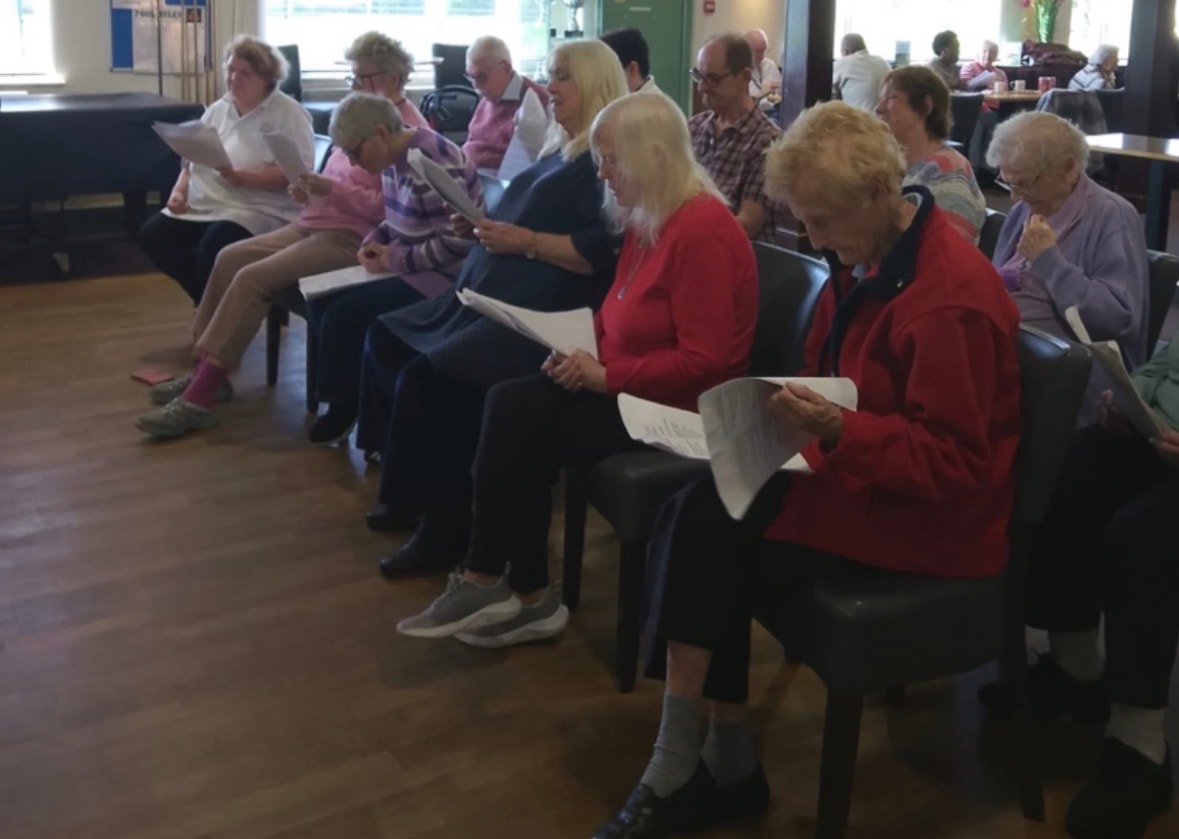 Older adults seated in a row reading sheets at a group session